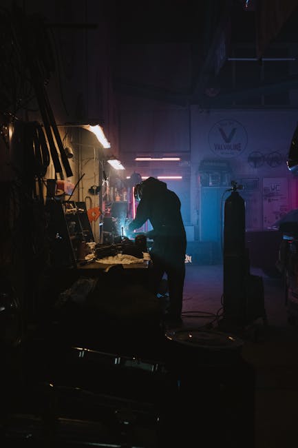 Silhouette of a welder working with sparks in a moody garage setting.